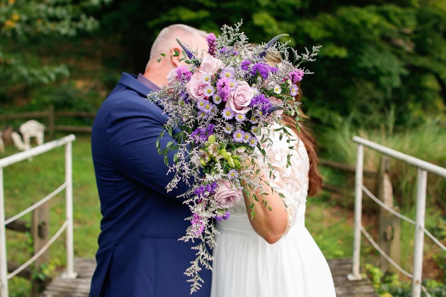 Newly married couple kissing behind a cascading purple and pink bridal bouquet